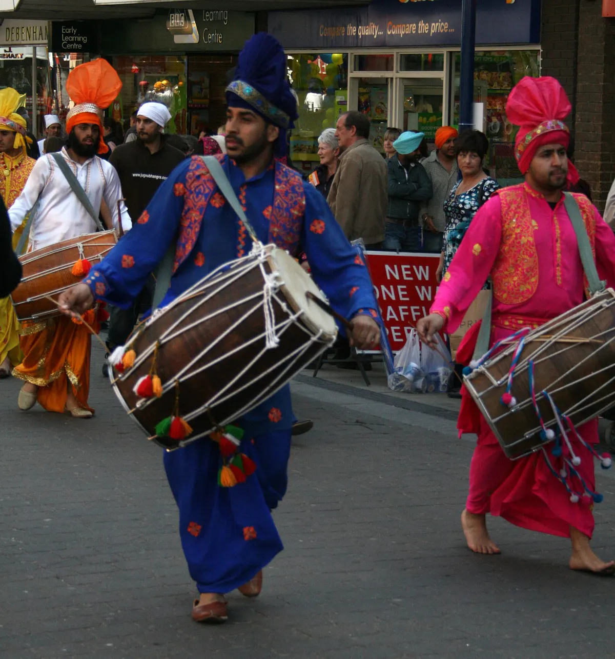 Dhol players in bright Punjabi outfits drumming in a Vaisakhi street parade