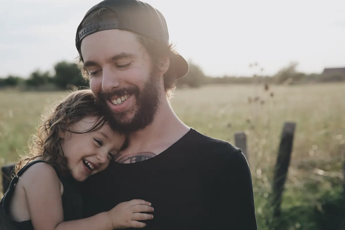 Father hugging his laughing daughter in a sunny field