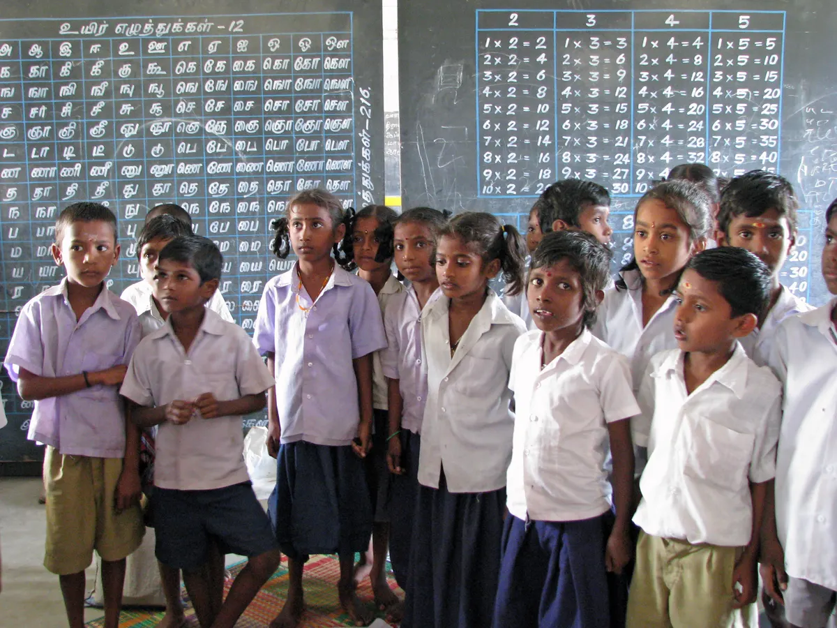 Group of Indian school children in uniform standing in front of a classroom blackboard