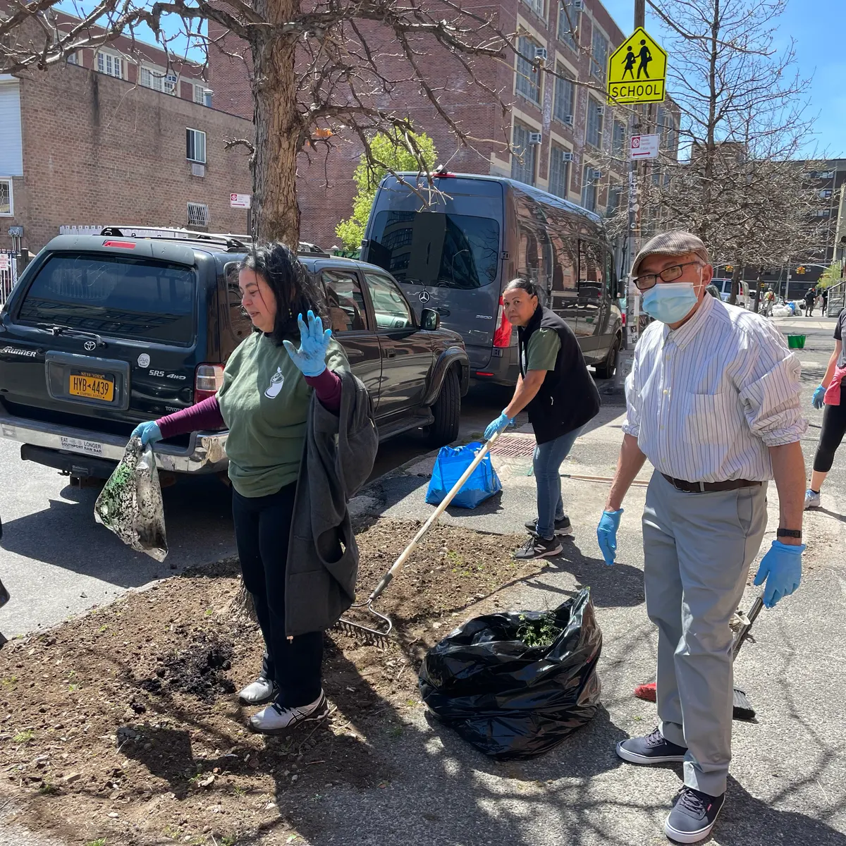 Volunteers with rakes and gloves clean up litter from a city street on Earth Day