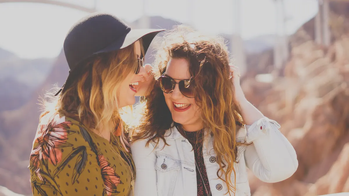 Two women friends laughing together outdoors on a sunny day