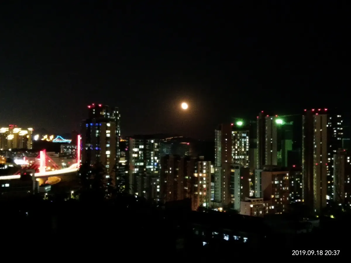 Full moon rising above city towers and their night lights