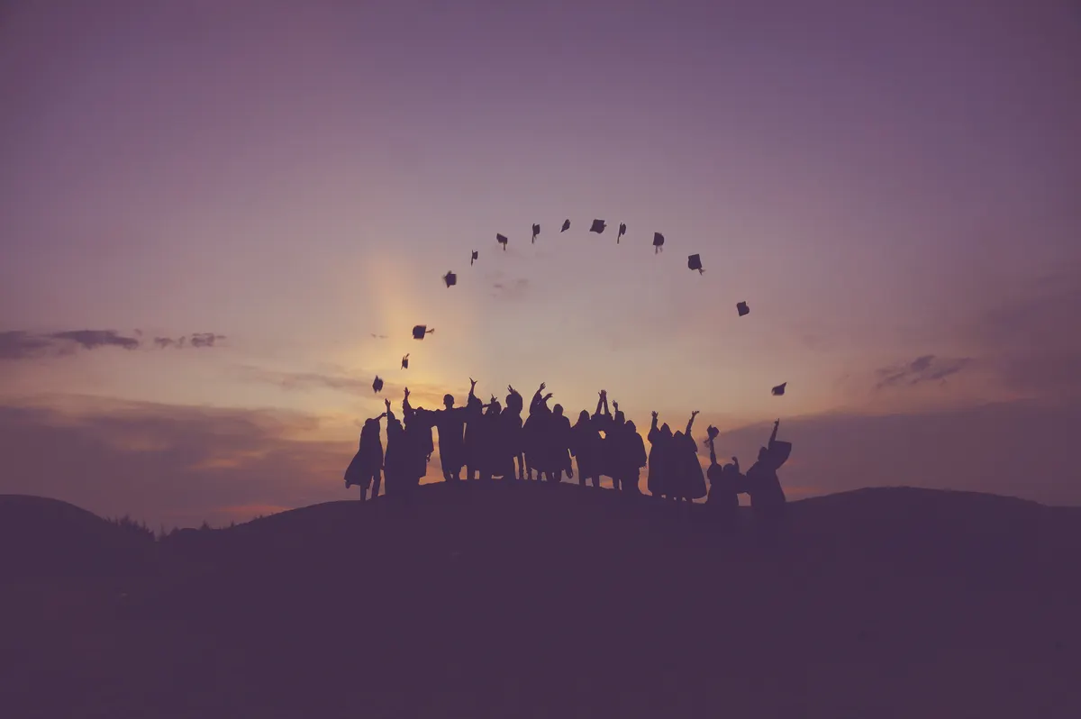 Silhouettes of graduates throwing their caps into a purple sunset sky