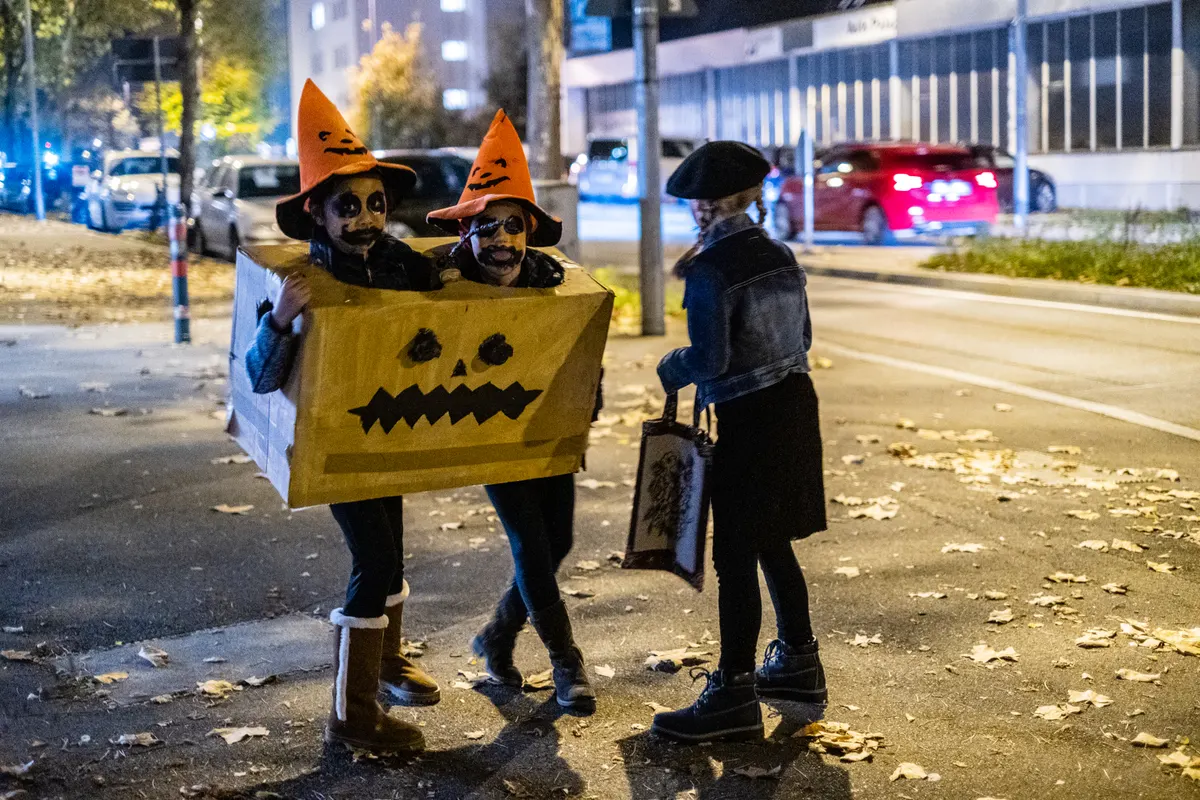 Kids in a homemade jack-o-lantern box costume and witch hats out trick-or-treating