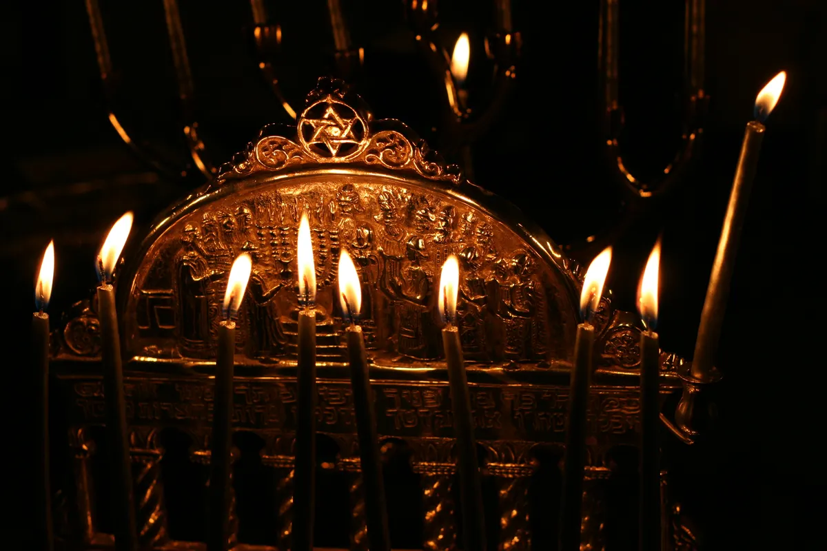 Brass Hanukkah menorah with all its candles lit in a dark room