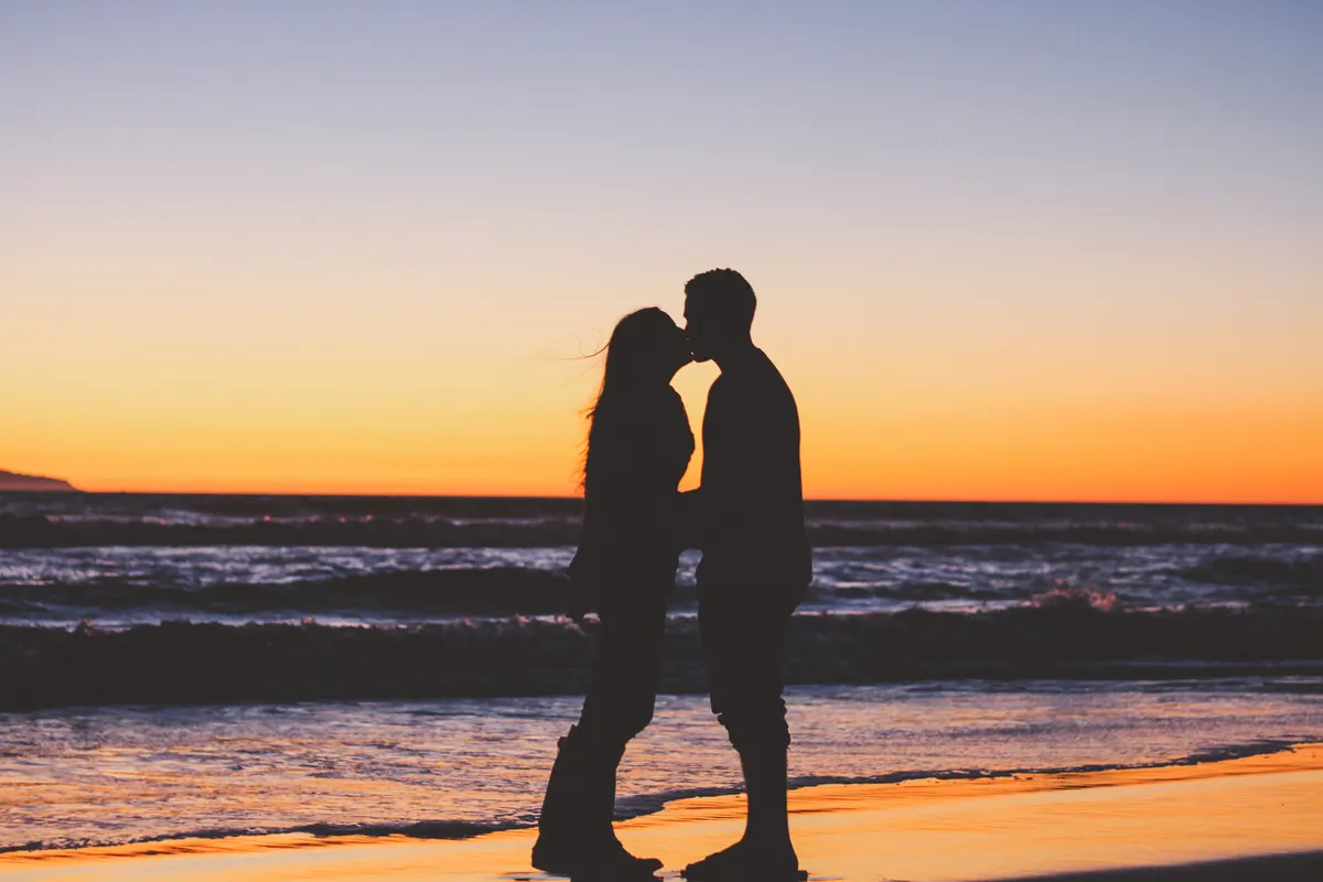 Silhouette of a couple sharing a kiss on a beach at sunset