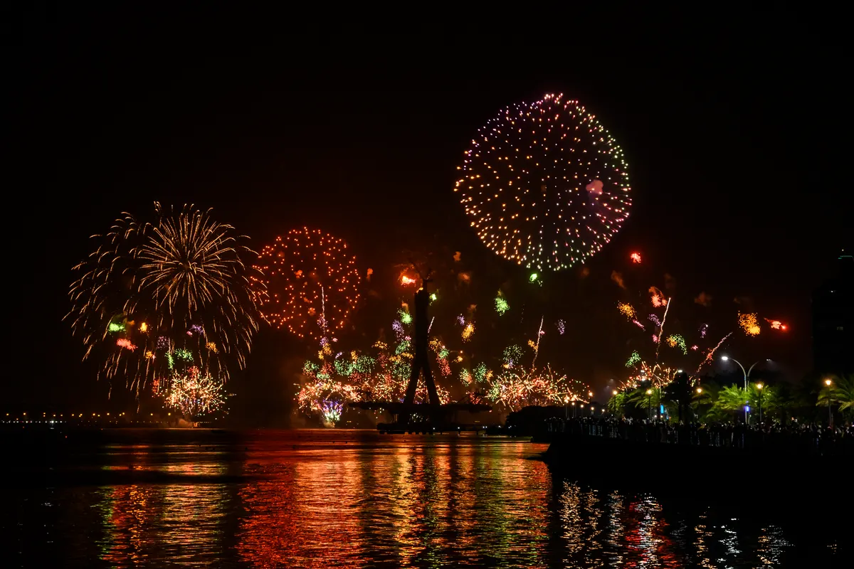 New Year fireworks over a harbour, their colours reflected in the water