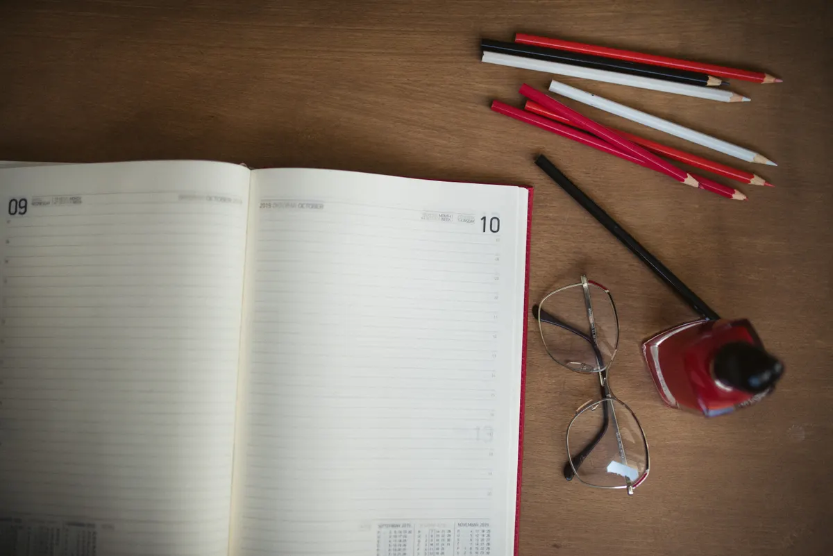 Open planner with coloured pencils and glasses on a wooden desk, ready for new plans