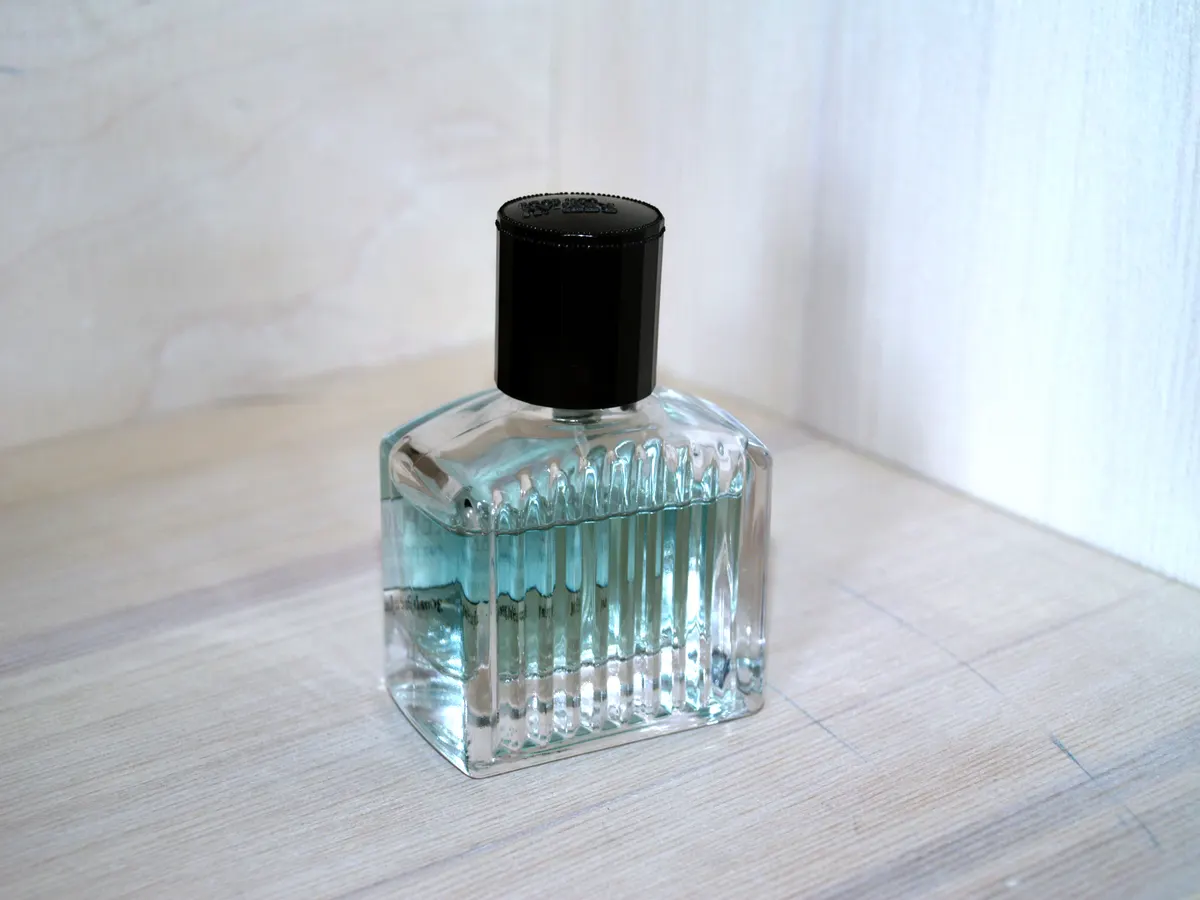 A glass perfume bottle with a black cap on a white table
