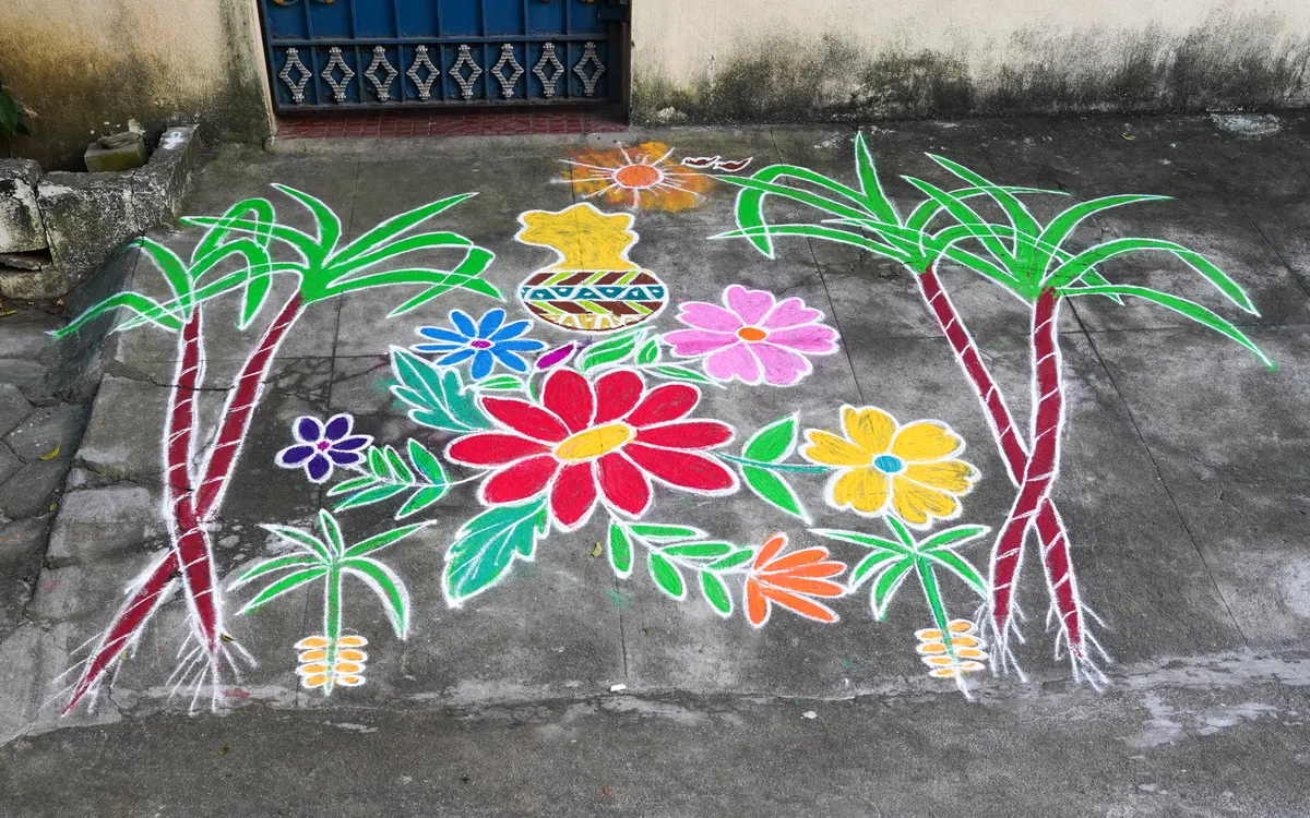 Colourful Pongal kolam with a clay pot, sugarcane and flowers drawn on a street