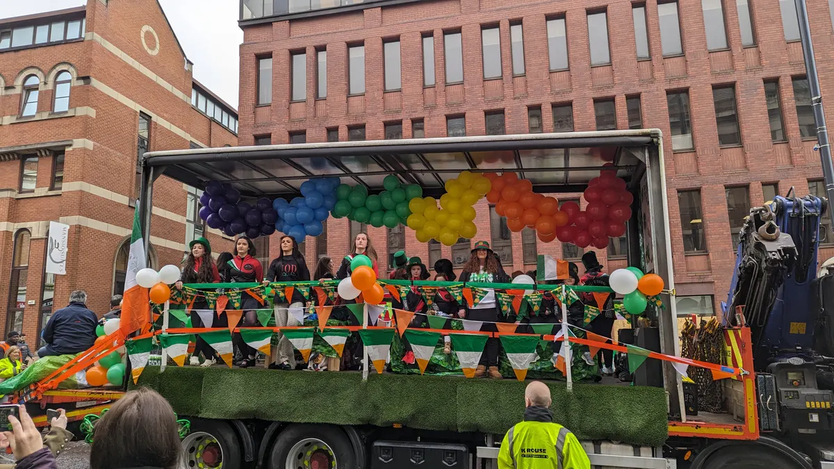 A St. Patrick's Day parade float with Irish flags and balloons on a city street