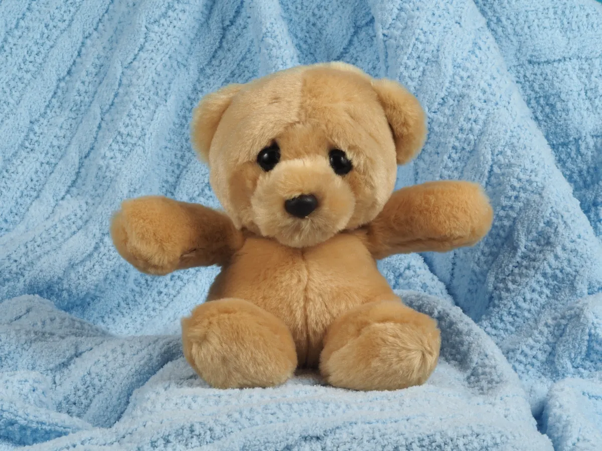 A soft brown teddy bear sitting on a blue knitted blanket