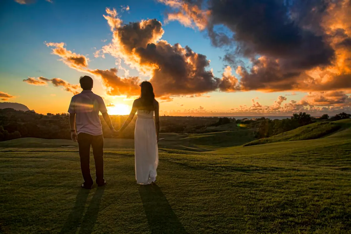 A couple holding hands and watching the sunset, seen from behind
