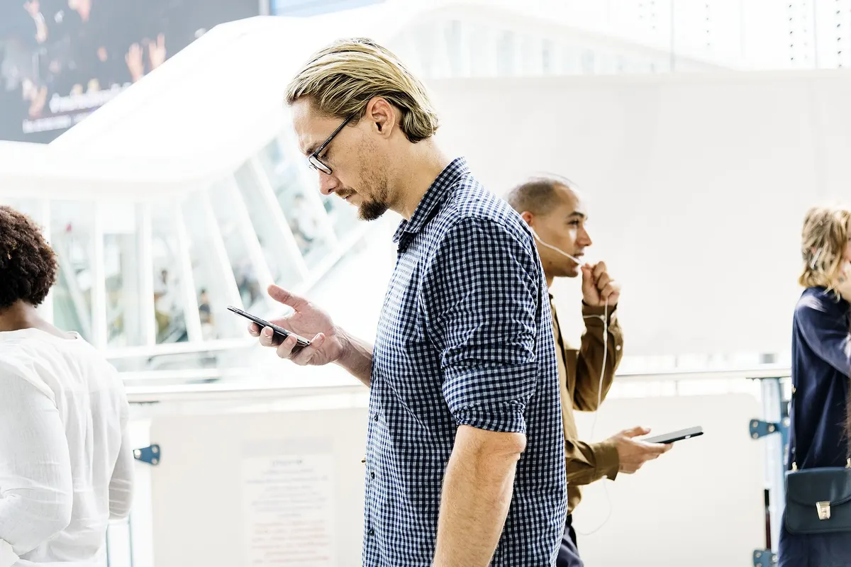 Young man reading his phone in a busy, sunlit hall