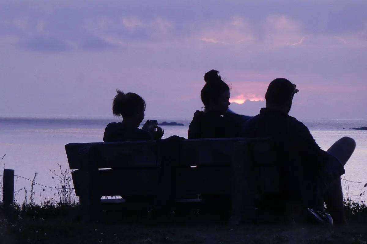 Friends silhouetted on a bench by the sea at dusk