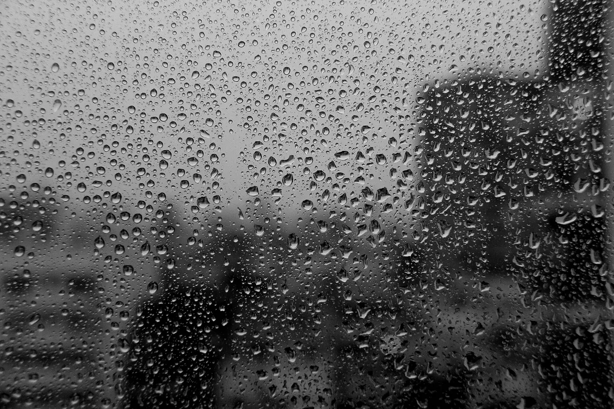 Rain drops running down a window with blurred city buildings behind