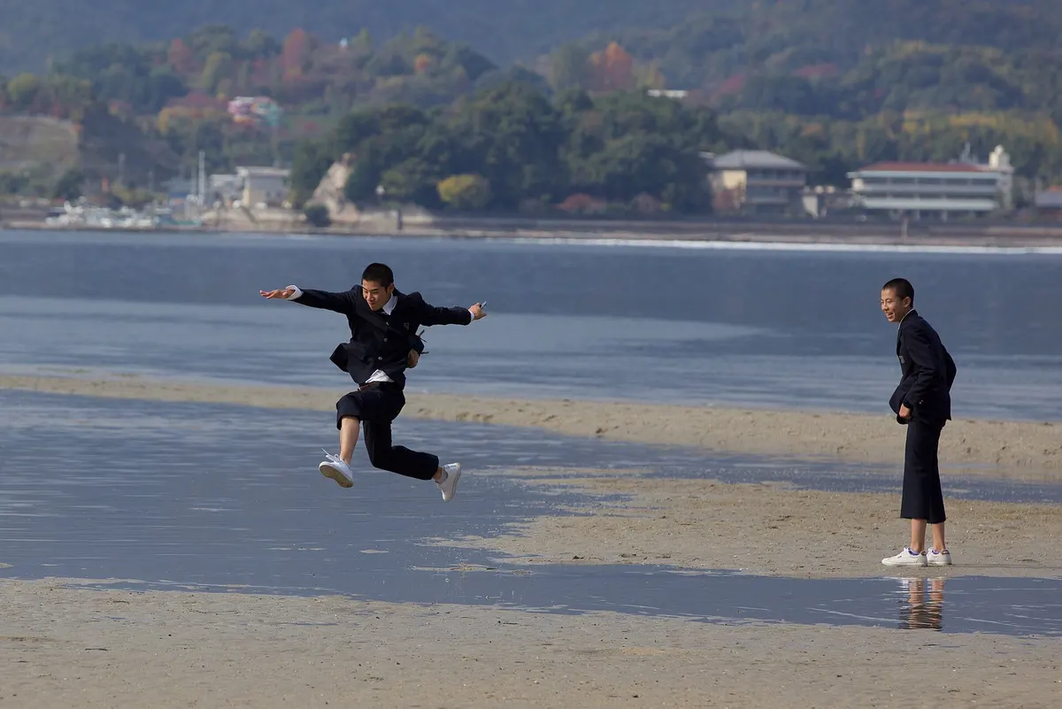 Young man leaping across a beach while his friend watches