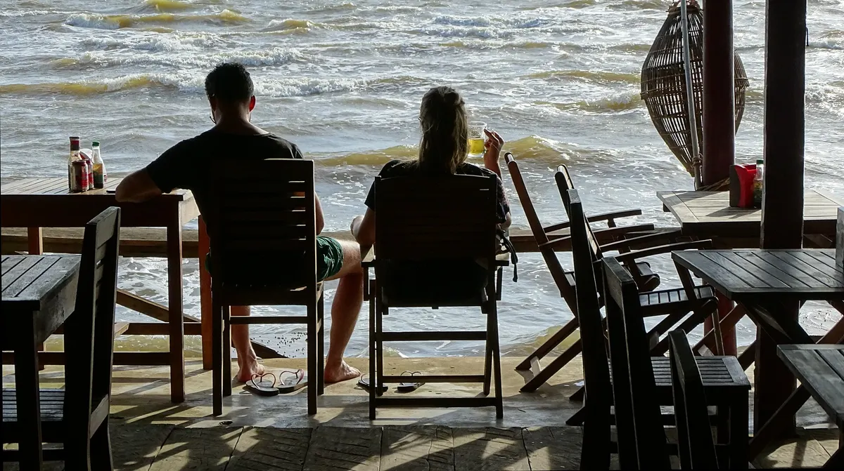 Couple sitting at a seafront restaurant looking out at the water in Kep, Cambodia