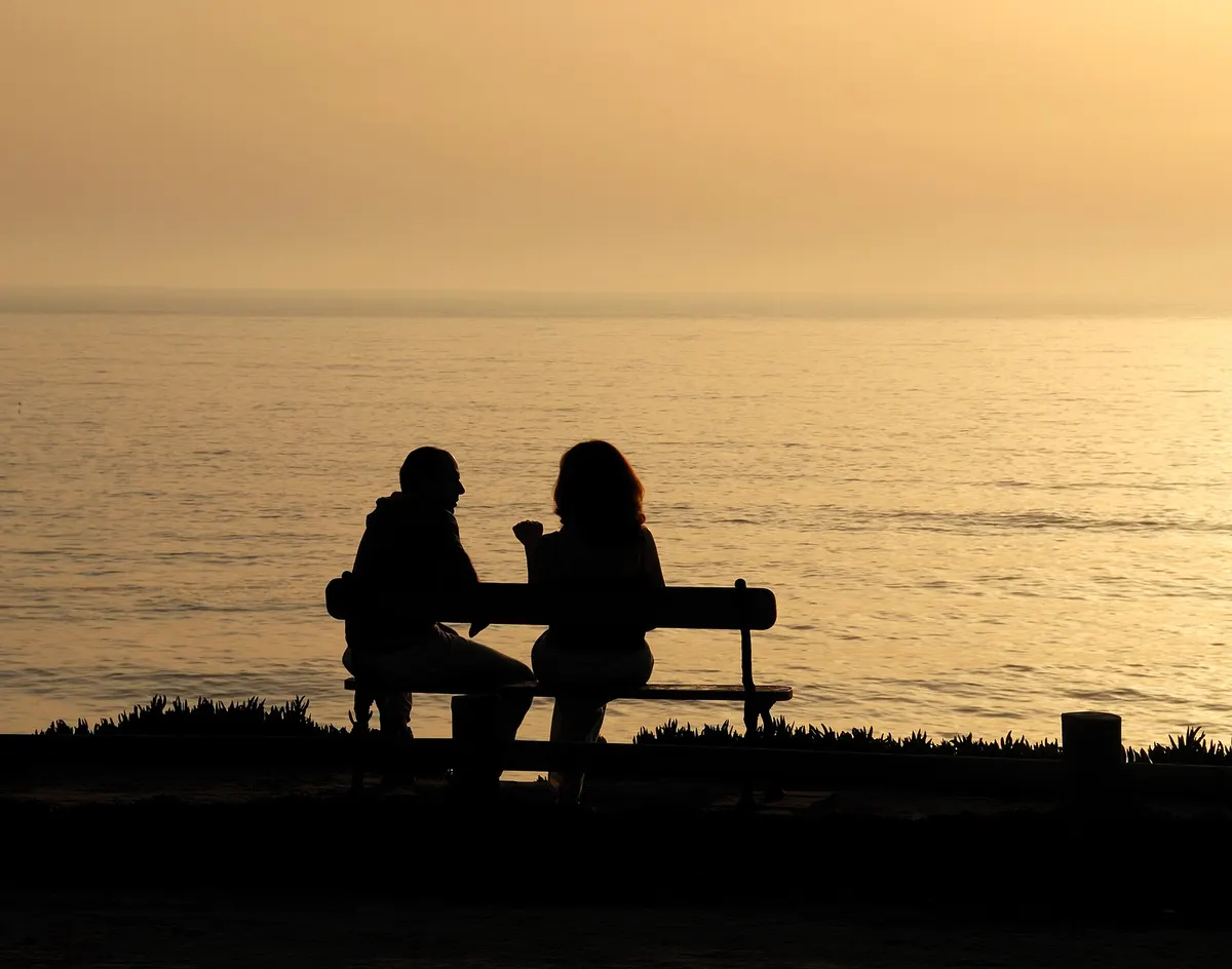 Couple silhouetted on a bench by the sea at sunset
