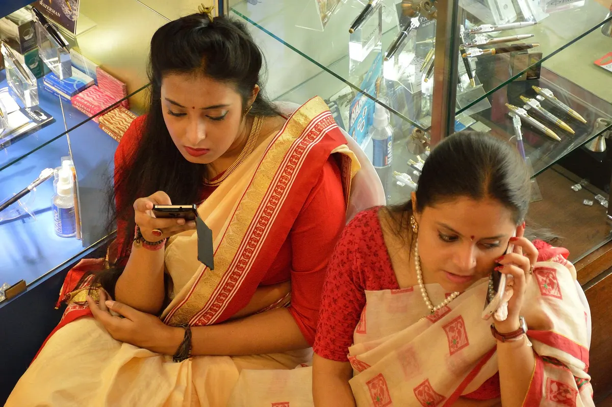 Two women in sarees looking at their phones