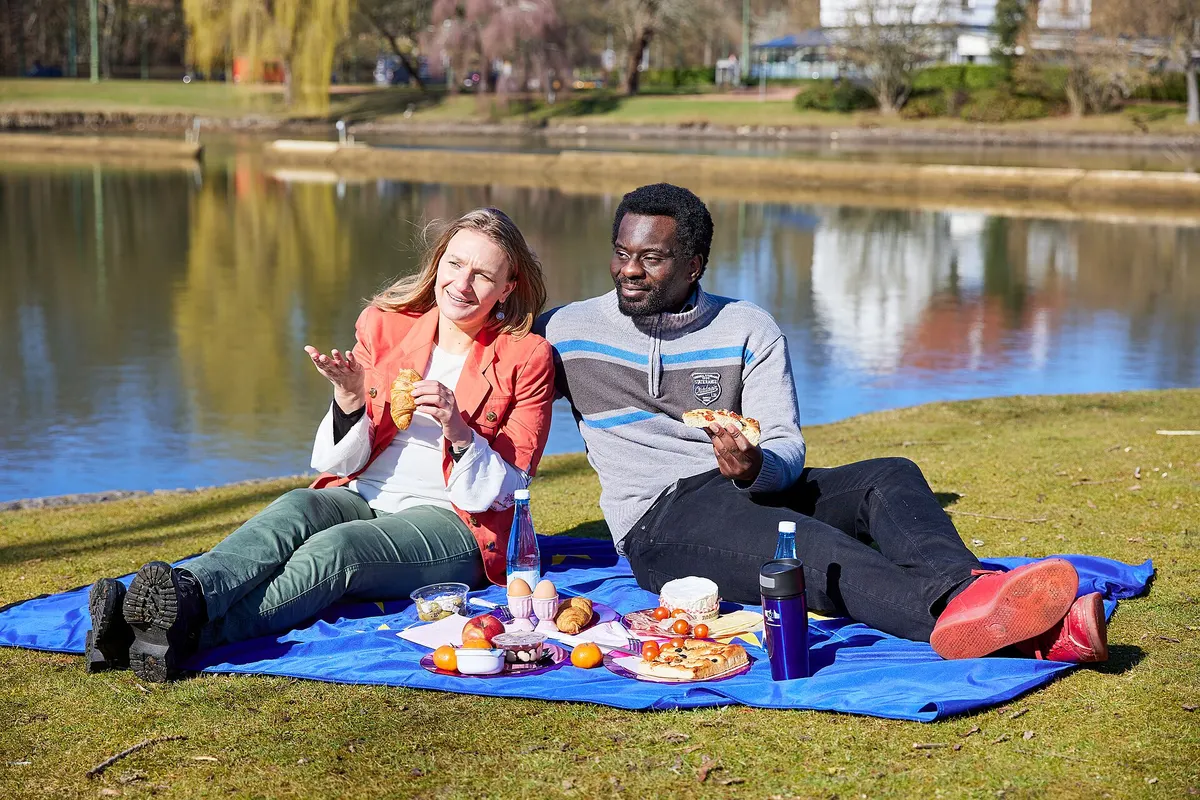 Couple having a picnic on a blue blanket beside a lake in a park