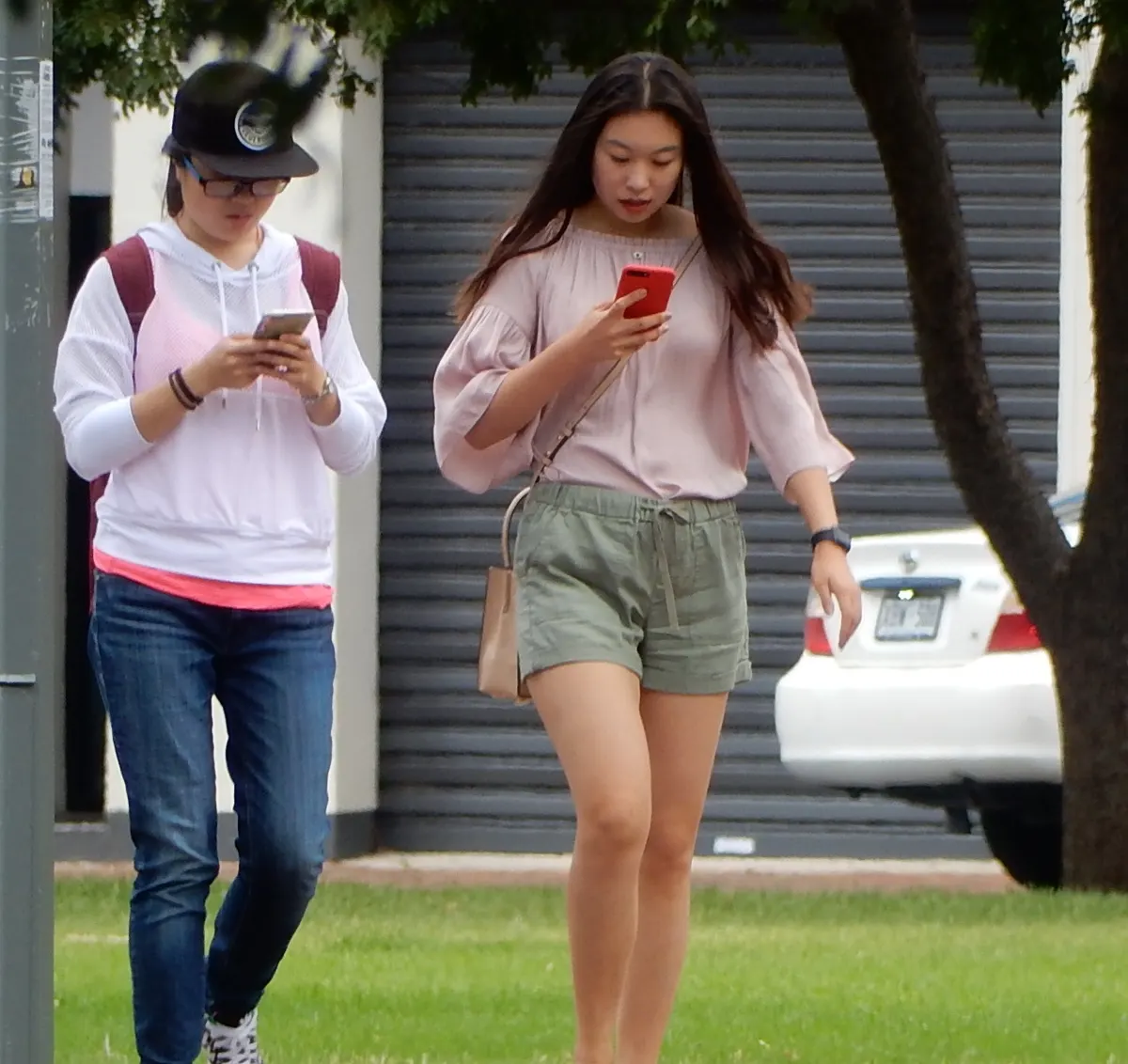 Two friends walking side by side, each looking at a mobile phone